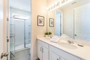 Une salle de bain moderne dotée d’une douche à parois de verre, d’un meuble-lavabo à deux vasques et d’un grand miroir.