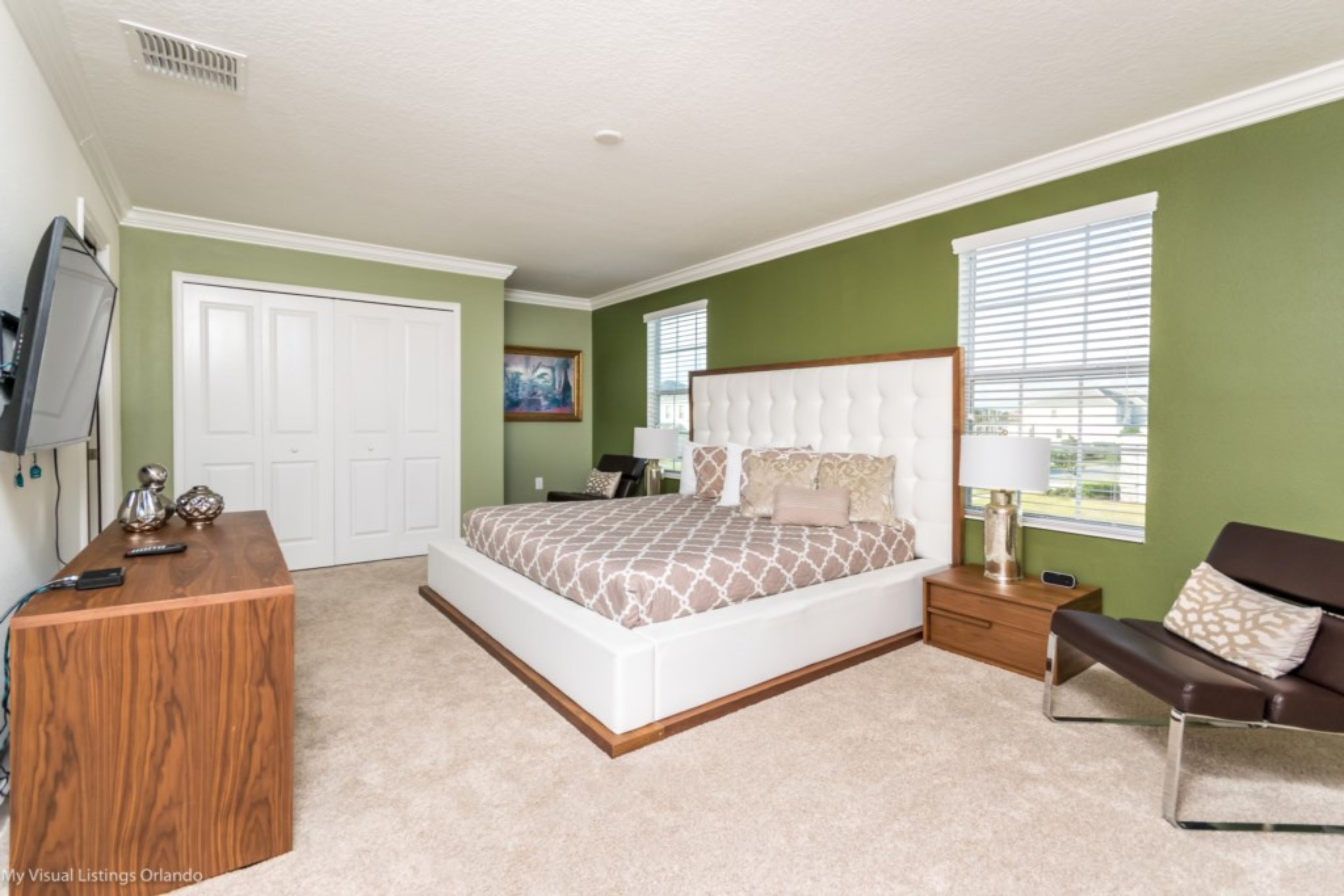 A bedroom with a large bed, a wooden desk, a TV, and a window with blinds.