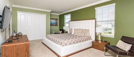A bedroom with a large bed, a wooden desk, a TV, and a window with blinds.
