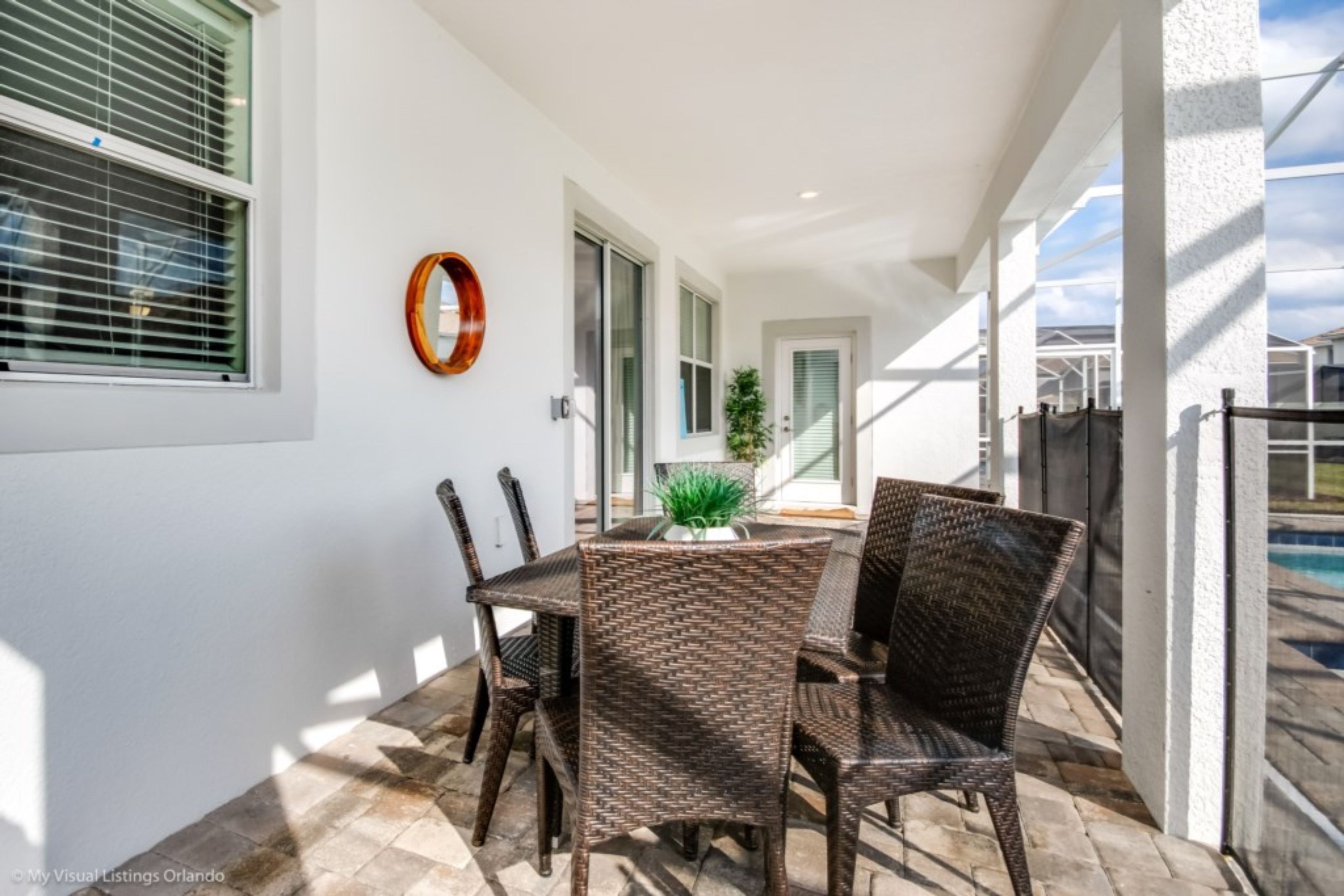 A covered patio with a dining table and chairs, a potted plant, and a view of a swimming pool.