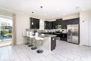 A modern kitchen with dark cabinets, stainless steel appliances, and a central island with bar stools.