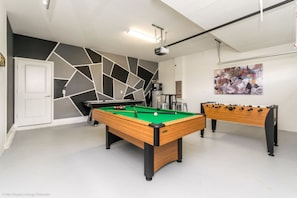 A pool table with a green felt surface, a foosball table, and a modern wall with geometric patterns.