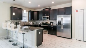 A modern kitchen with dark cabinets, stainless steel appliances, and a central island with bar stools. - 9020hs (Davenport)