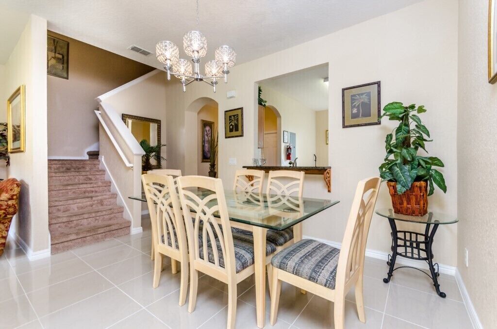 Un comedor con una mesa de vidrio, sillas de madera, una araña y una escalera que lleva a otra habitación.