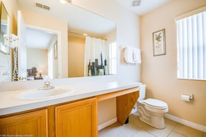 A bathroom with a white sink, wooden vanity, a toilet, and a large mirror. - 734lam Regal Palms Town Home (Davenport)