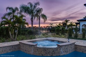 A hot tub with a stone surround, surrounded by palm trees and a fence. - 7 Bdrmstheatergamermpoolmansion (Kissimmee)