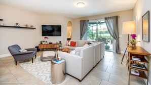 A modern living room with a sofa, armchair, and a TV mounted on the wall. - 5 Bedroom 5 Bathroom Solterra Resort Luxury Villa (Davenport)