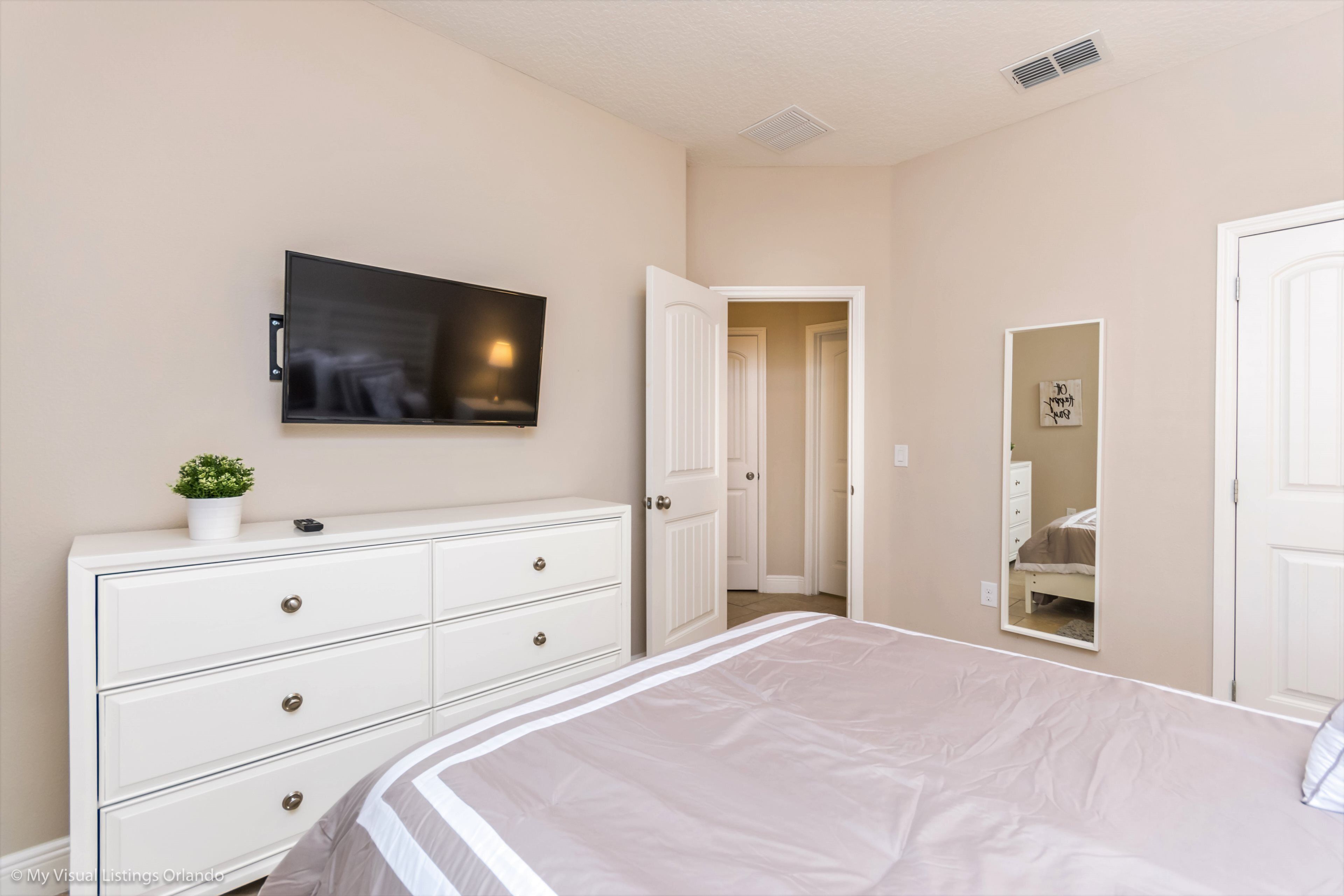 A bedroom with a bed, a dresser, a TV, a door, and a mirror.