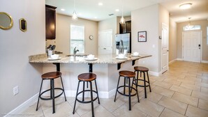 A kitchen with a central island, bar stools, and a refrigerator. - 5 Bedroom 5 Bathroom Solterra Resort Luxury Villa (Davenport)