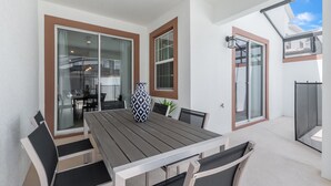 Eine moderne Terrasse mit Holztisch und -stühlen, großen Schiebeglasfenstern und Blick ins Innere.