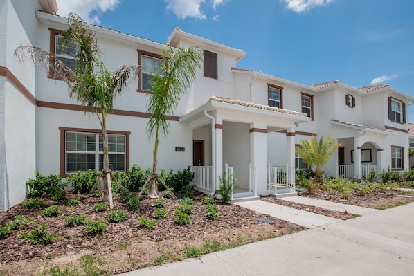 A row of townhouses with a covered front porch, a landscaped garden, and a clear blue sky.
