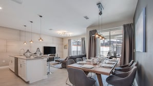 Eine moderne Küche mit einer zentralen Kochinsel, ein Essbereich mit einem langen Tisch und Stühlen sowie eine Wohnbereich mit einer Couch und Fernseher.