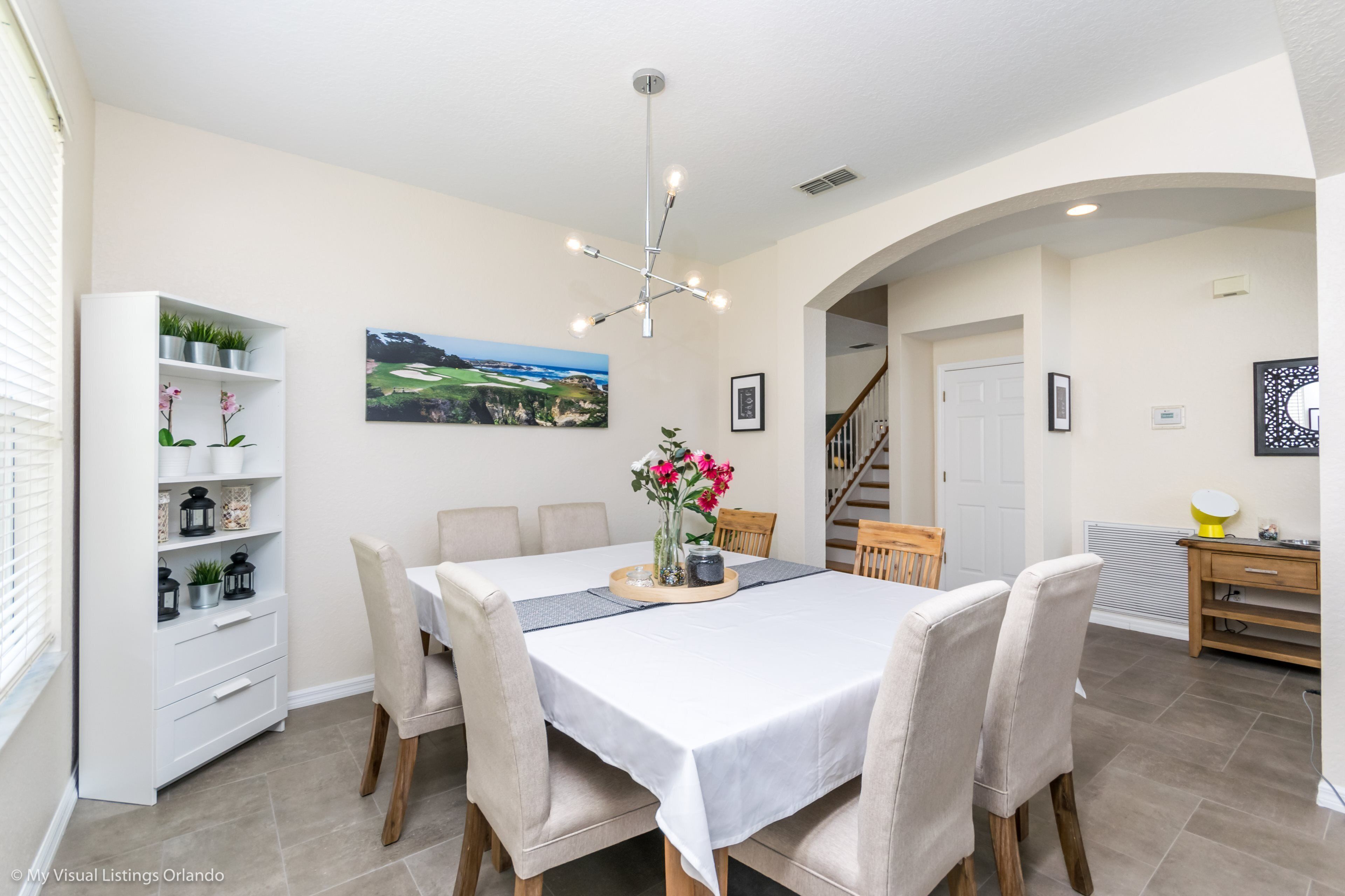 A dining area with a white table, beige chairs, a chandelier, and a view of a golf course through a window.