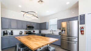 A modern kitchen with grey cabinets, stainless steel appliances, a wooden island with bar stools, and a pendant light.
