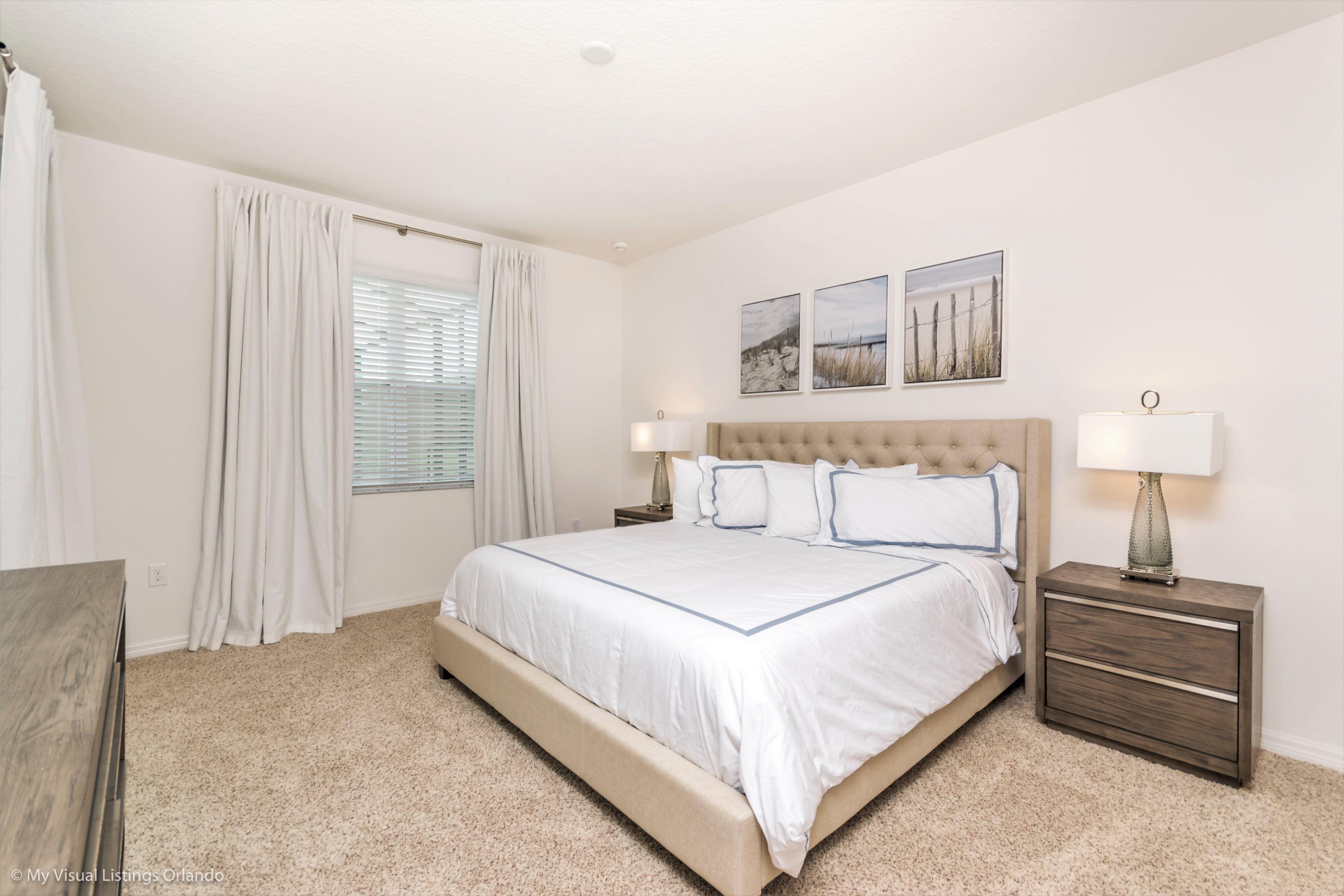 A bedroom with a large bed, two bedside tables, a nightstand, and a window with curtains.
