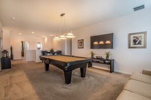 A living room with a pool table, a sofa, a TV, and a small bar area.