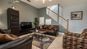 A living room with a brown leather sofa, a glass coffee table, a TV, and a staircase with wooden railings. - 322vvl (Davenport)