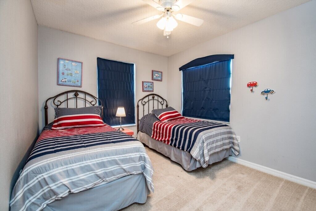 A bedroom with two beds, a ceiling fan, and a window with curtains.