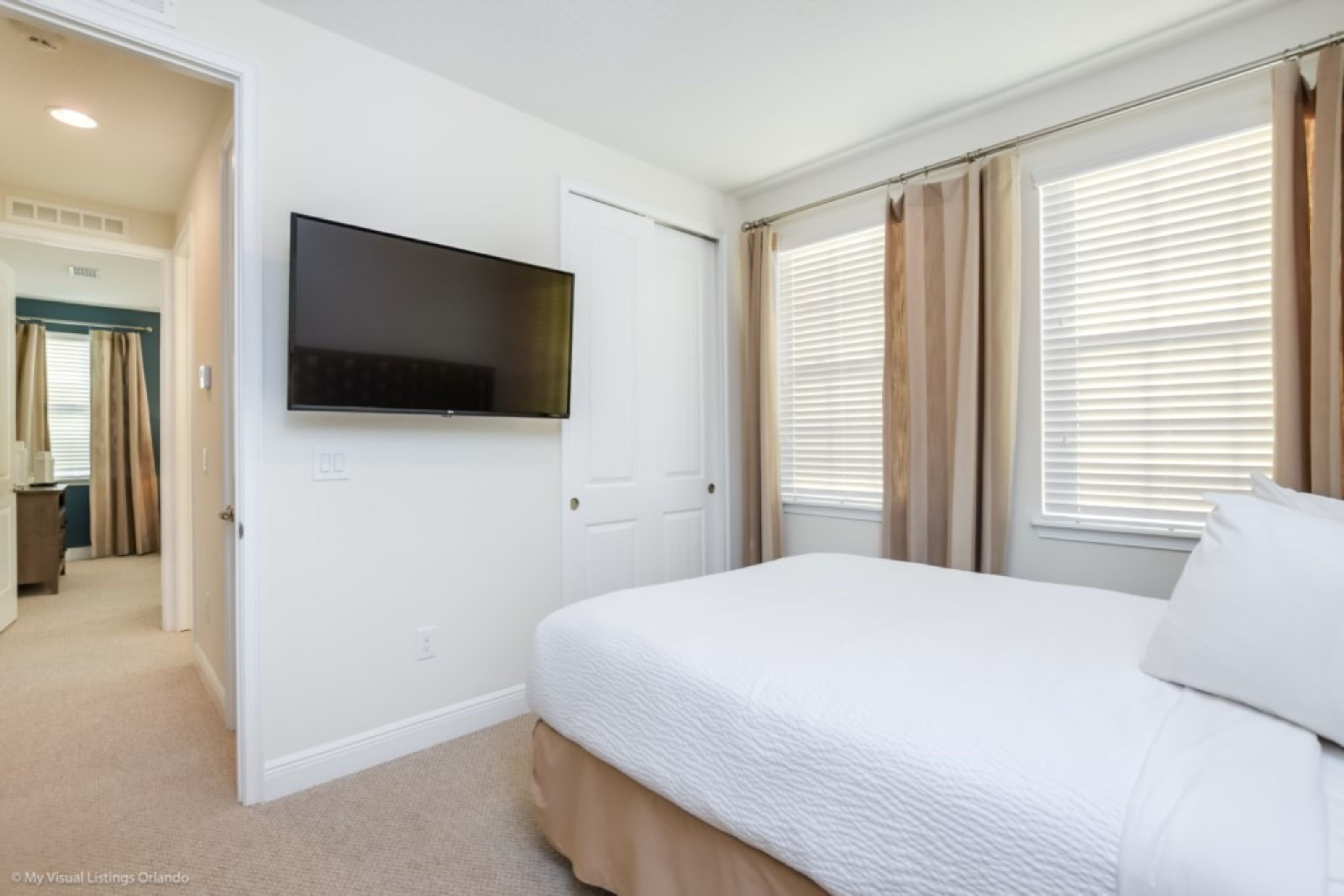 Un dormitorio con cama, televisor montado en la pared y ventana con cortinas.