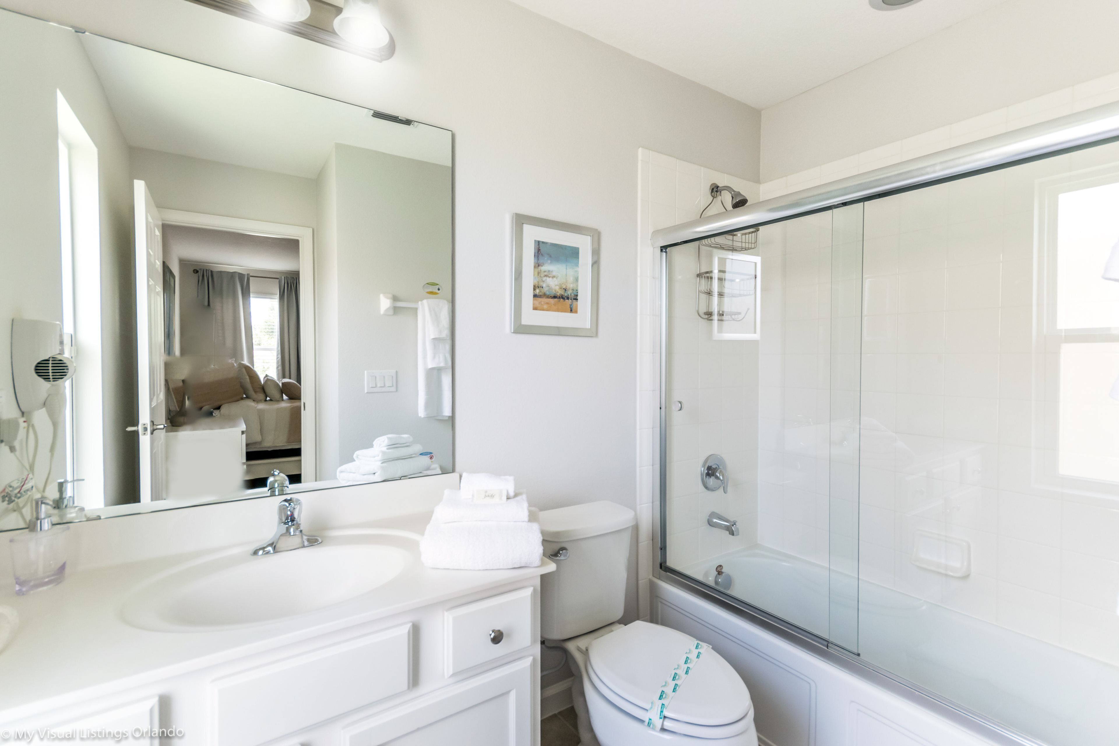 A bathroom with a large mirror, a sink, a toilet, and a glass-enclosed shower.