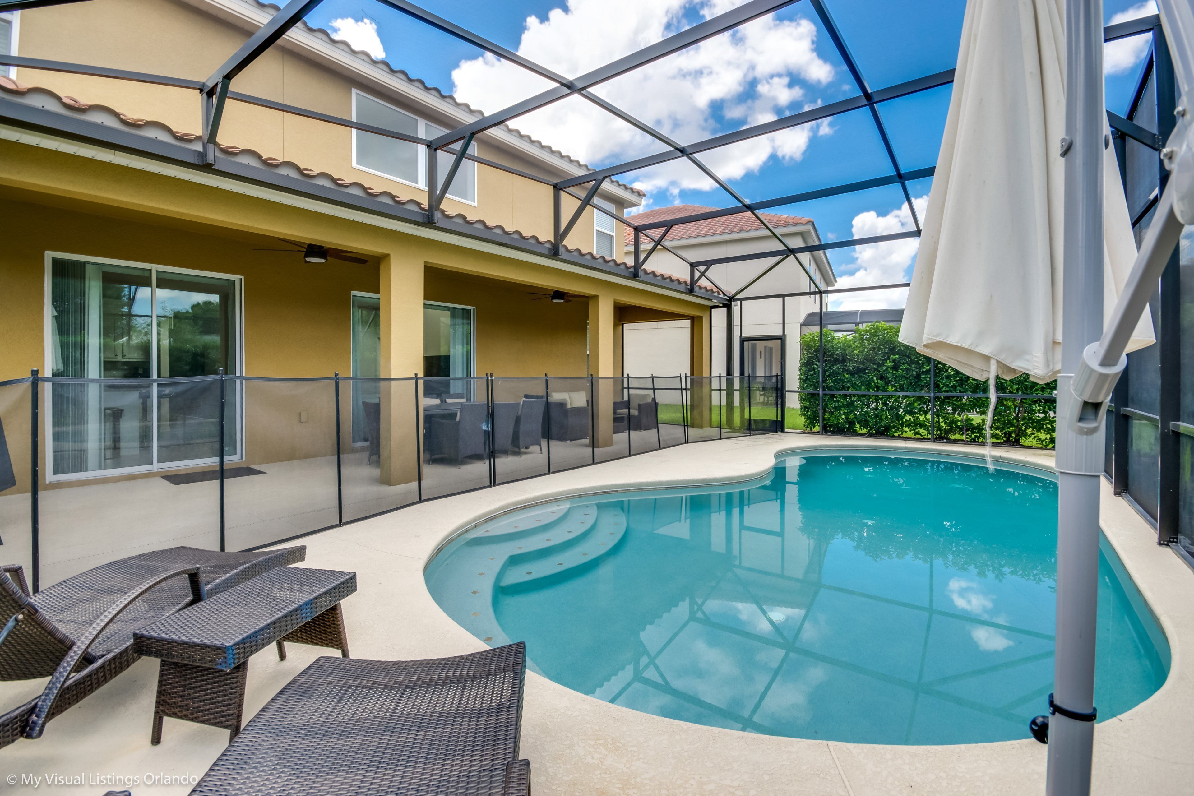 A swimming pool with lounge chairs, a covered patio, and a glass-enclosed structure.
