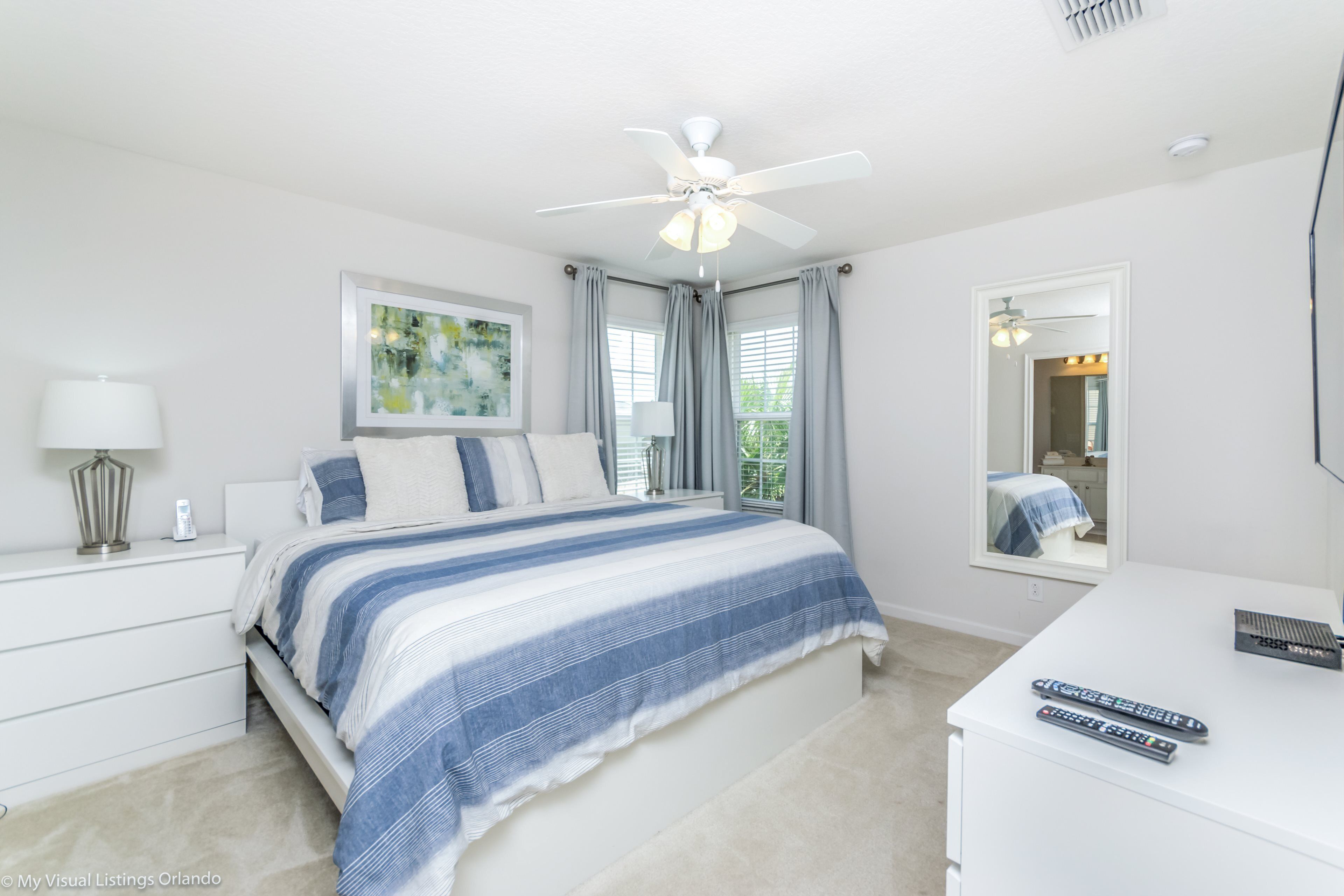 A bedroom with a bed, a nightstand, a desk, and a ceiling fan.
