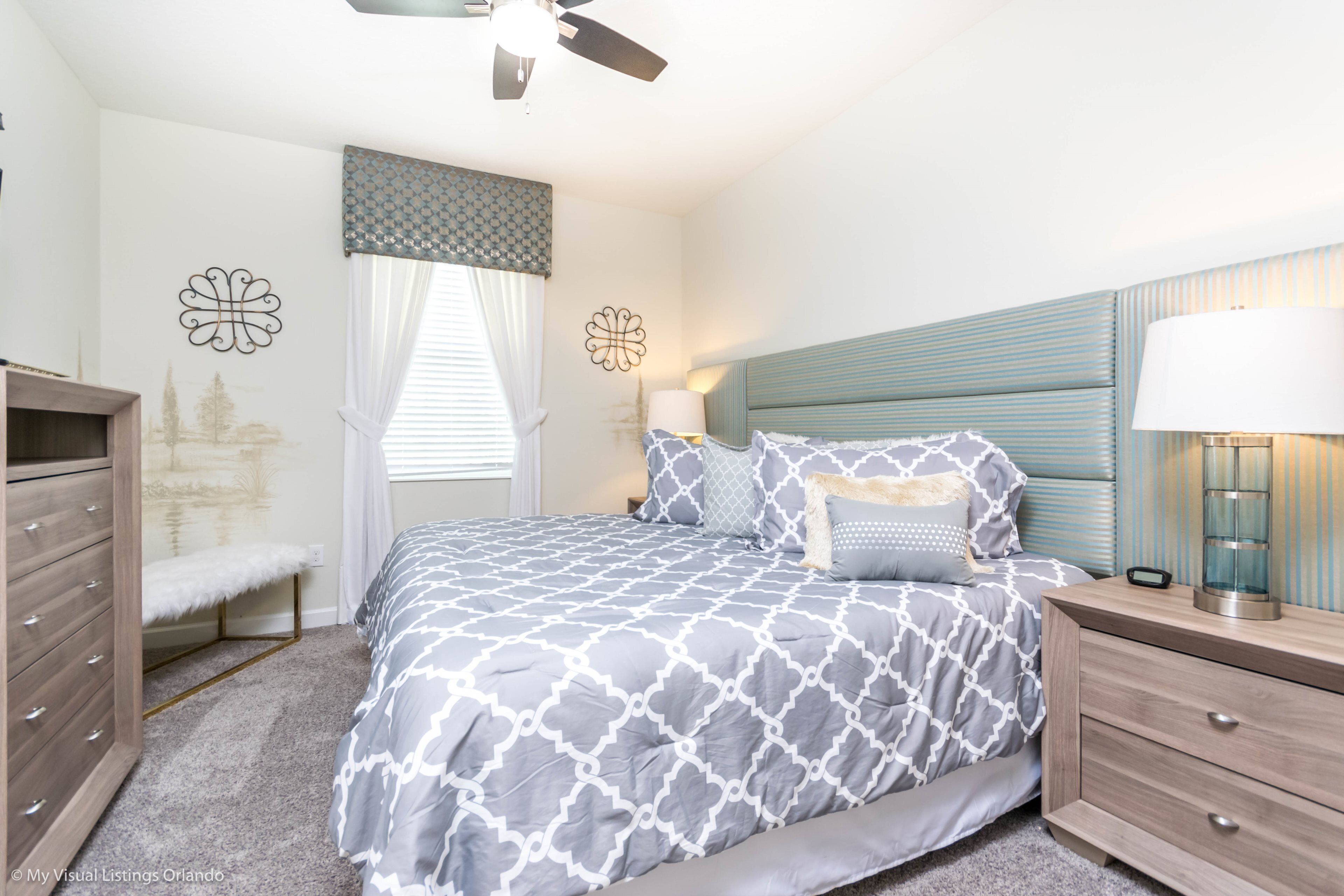 A bedroom with a bed, nightstands, a dresser, a ceiling fan, and decorative wall art.