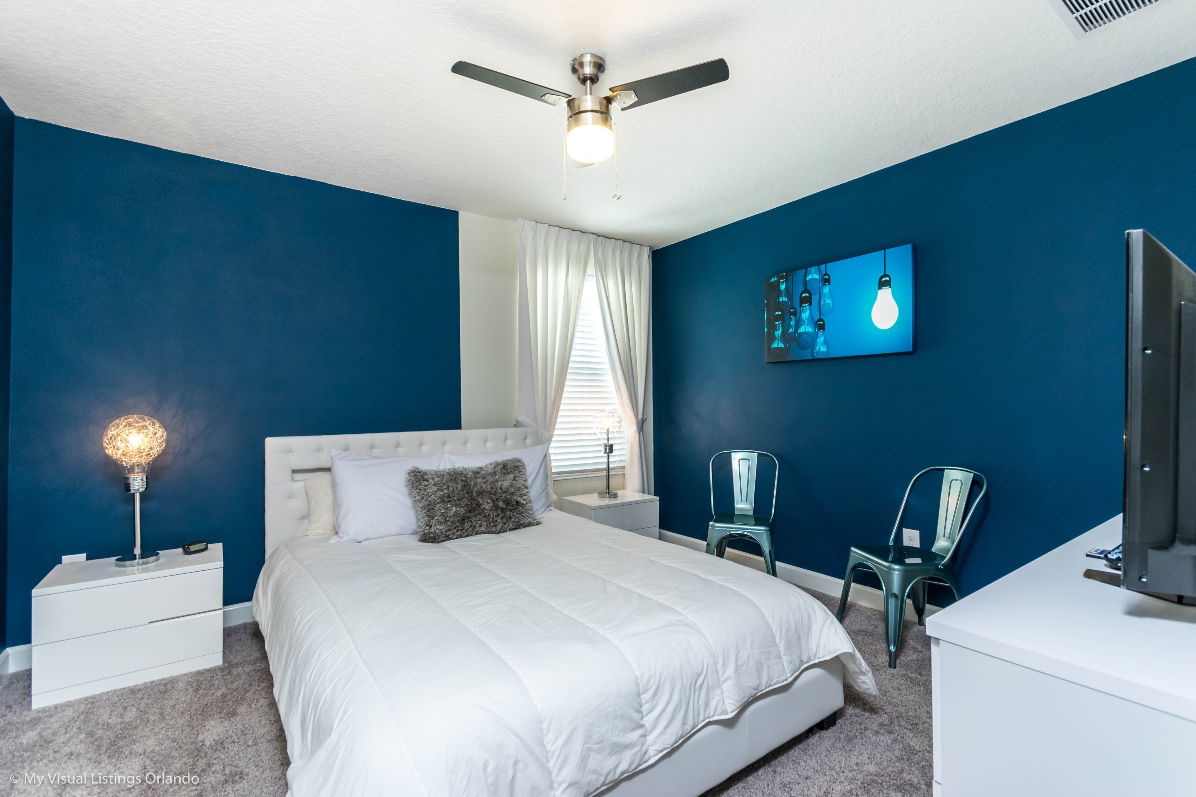 Ein Schlafzimmer mit Bett, Nachttisch, Stuhl, Fernseher und Deckenventilator.