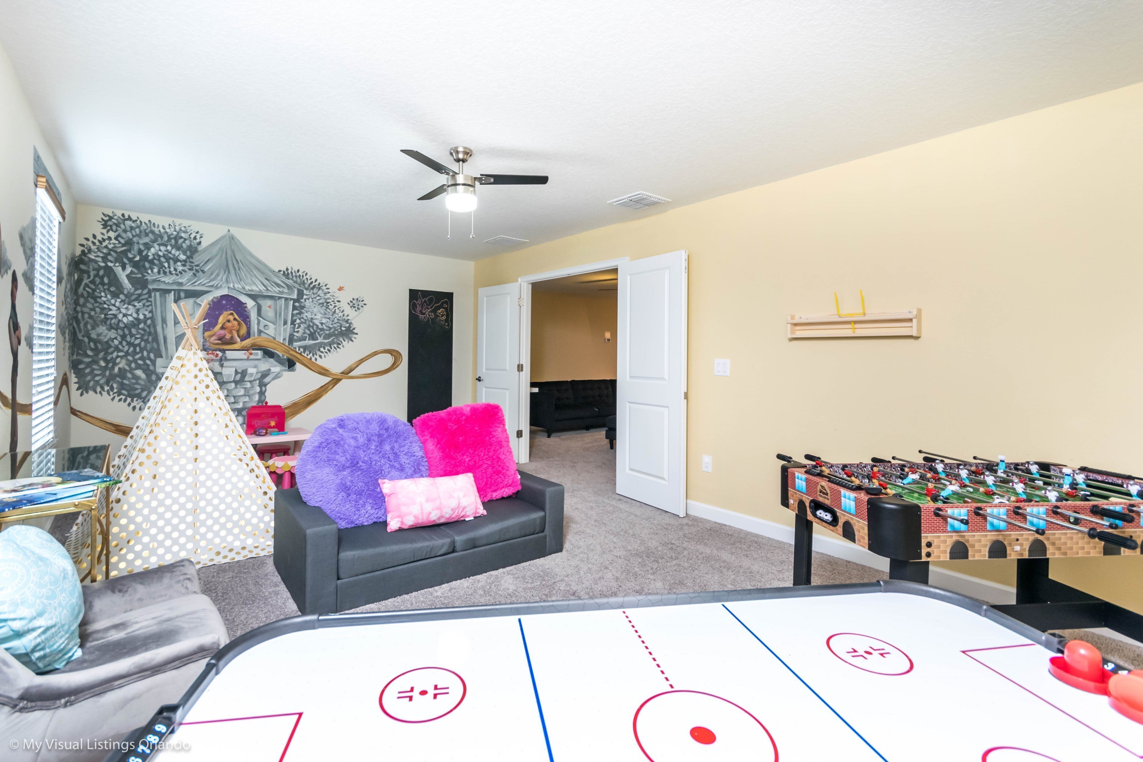 A living room with a foosball table, a shuffleboard table, and a sofa with colorful pillows.