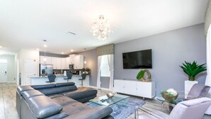Een moderne woonkamer met een hoekbank, een glazen salontafel en een flatscreen televisie aan de wand.