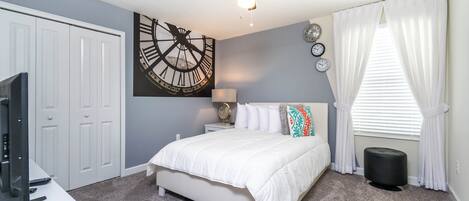 A bedroom with a bed, a ceiling fan, a clock, and a window with curtains.