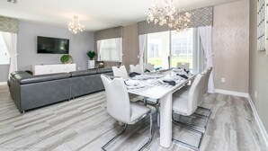 Een moderne eetruimte met een lange tafel, witte stoelen en een kroonluchter.