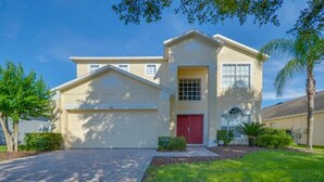 A two-story house with a garage, a red door, and a small garden with palm trees. - 616bd (Davenport)