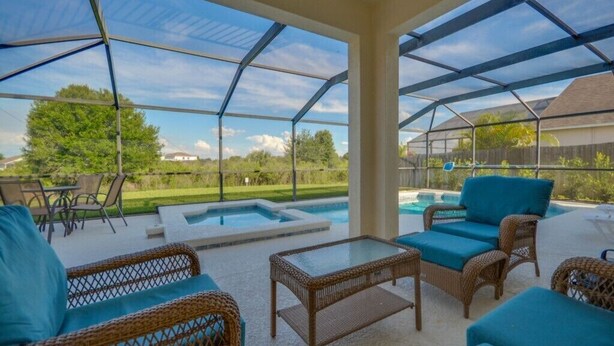 A covered outdoor patio with wicker furniture, a glass table, and a hot tub. - 616bd (Davenport)