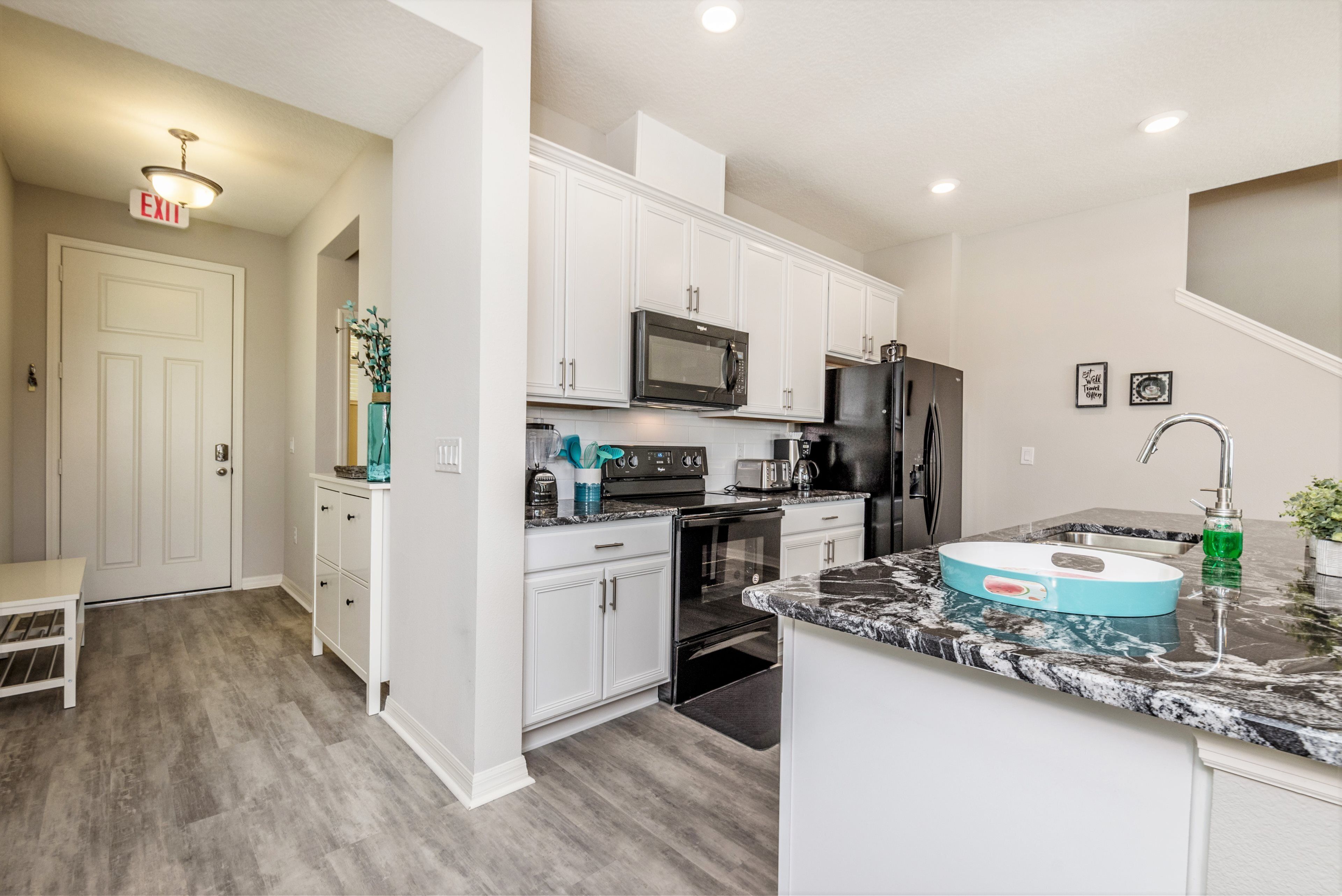 A modern kitchen with white cabinets, a black microwave, a stainless steel refrigerator, and a granite countertop.