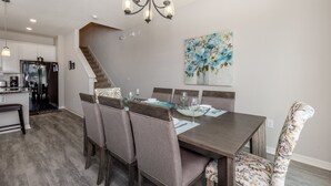 Een moderne eethoek met een donker houten tafel, comfortabele stoelen en een kroonluchter.