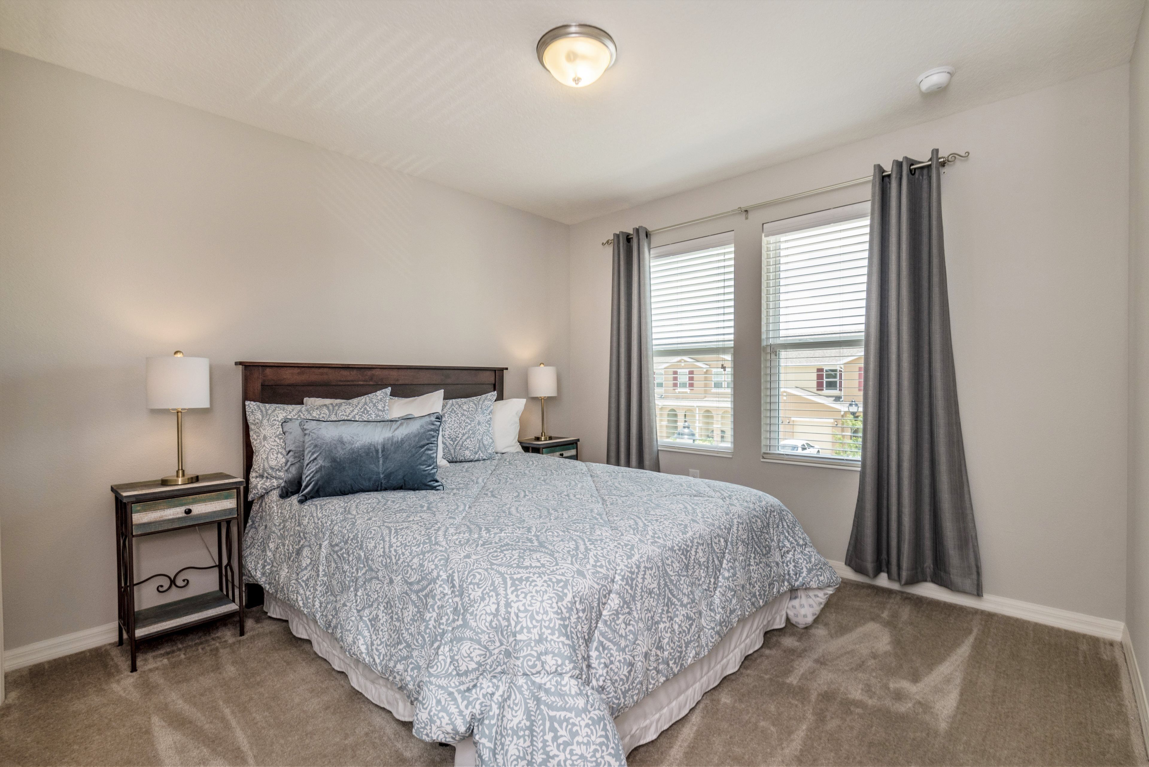 A bedroom with a large bed, two bedside tables with lamps, a headboard, and a window with curtains.