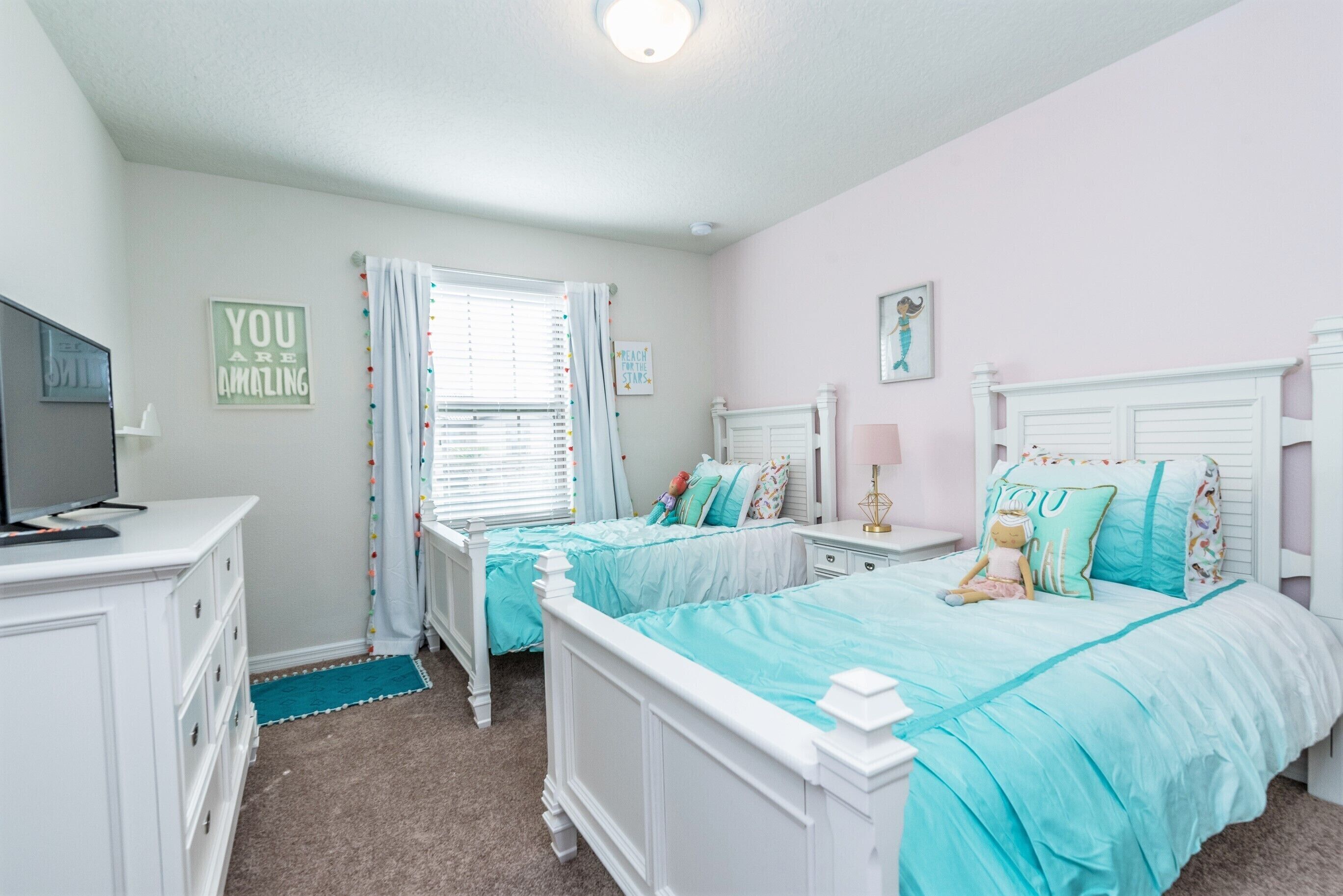A bedroom with two beds, a dresser, a TV, and a window with curtains.