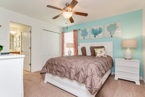Une chambre à coucher avec un lit, une table de chevet, un ventilateur de plafond et des œuvres d’art murales.