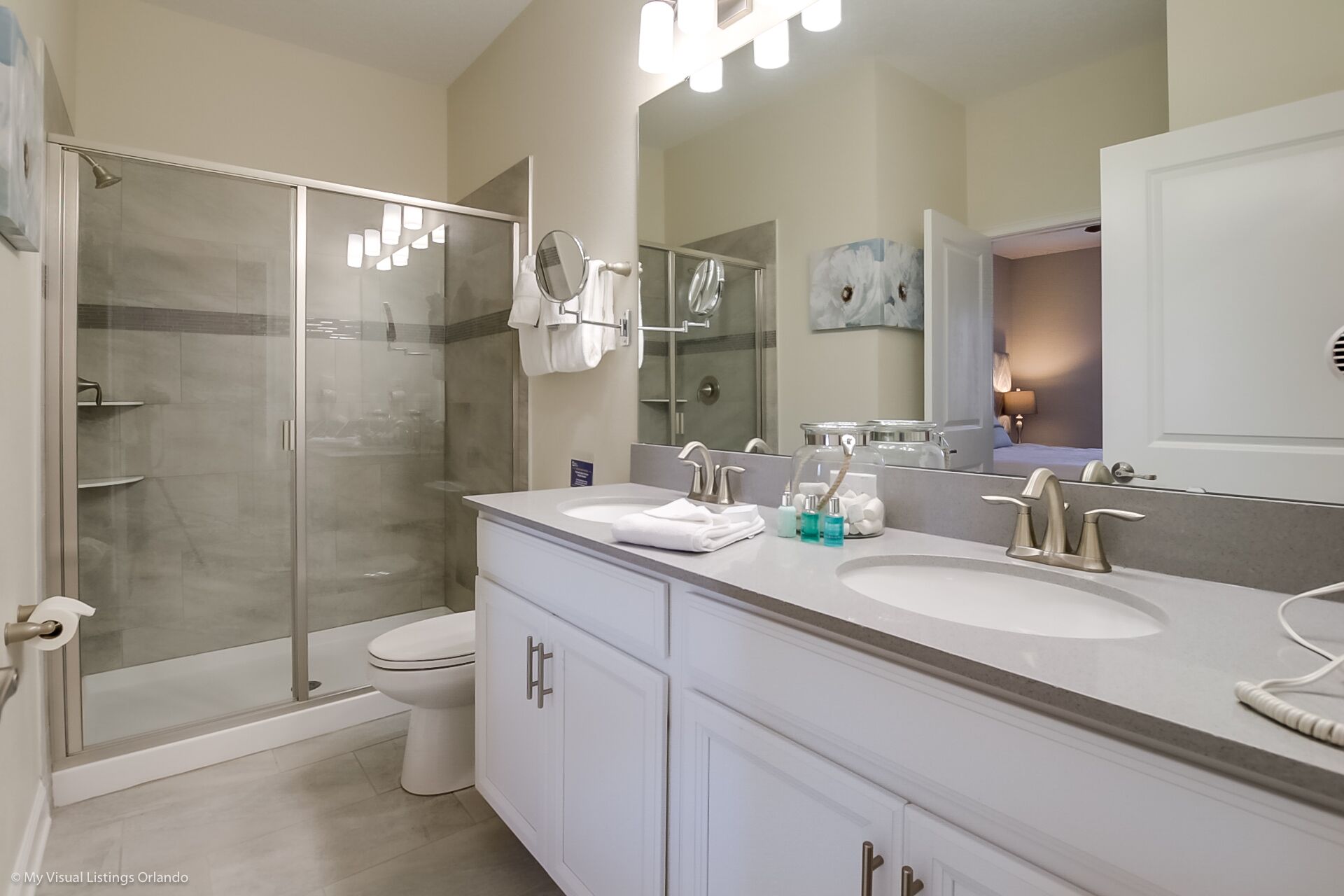 A modern bathroom with a glass-enclosed shower, dual sinks, and a large mirror.