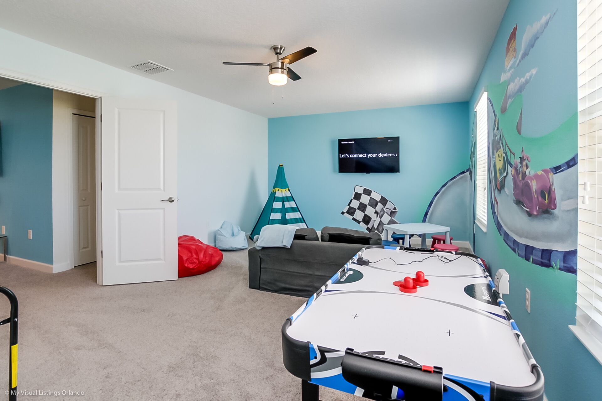 A room with a pool table, a ceiling fan, a TV, and a mural on the wall.
