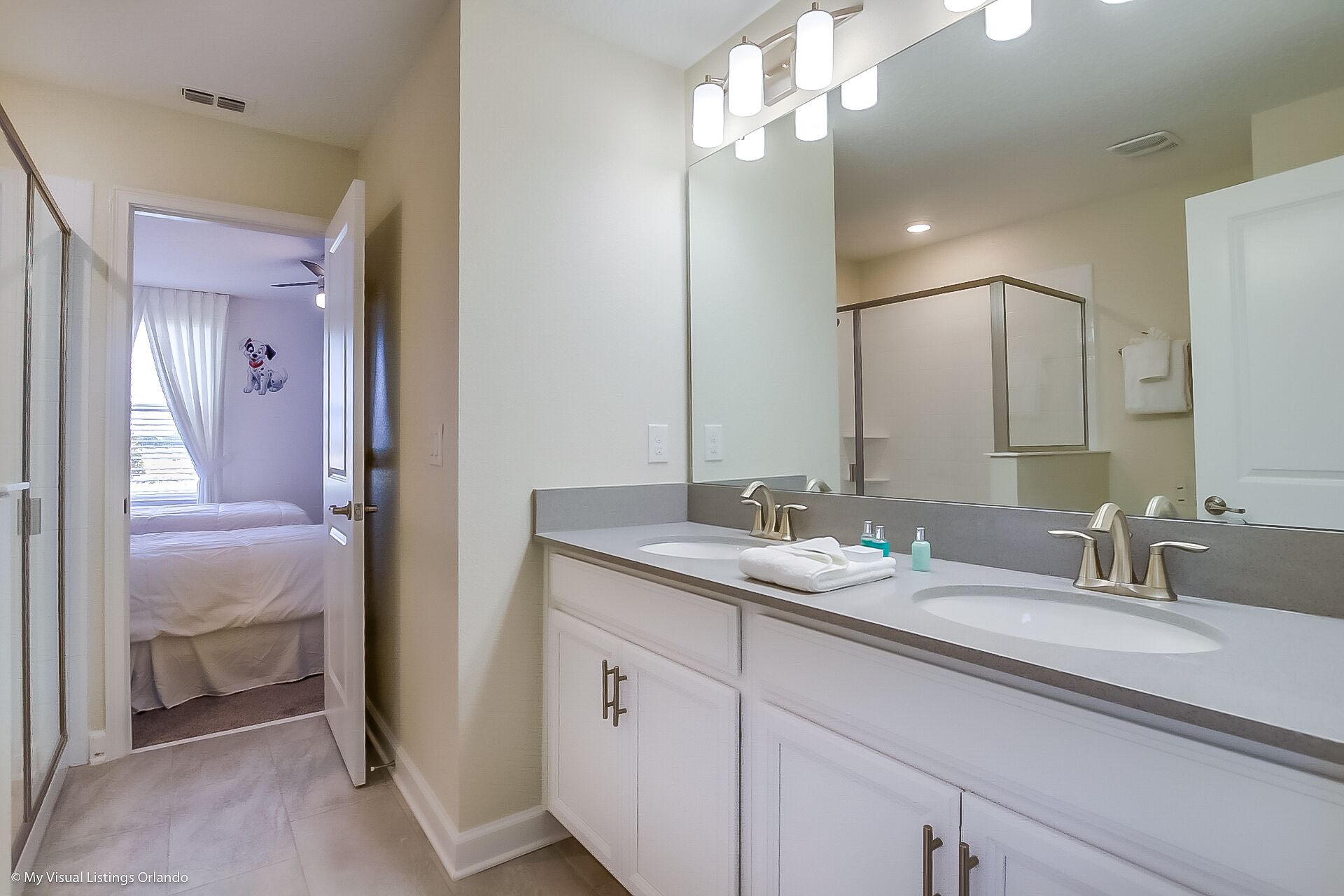 A modern bathroom with two sinks, a large mirror, and a walk-in shower.