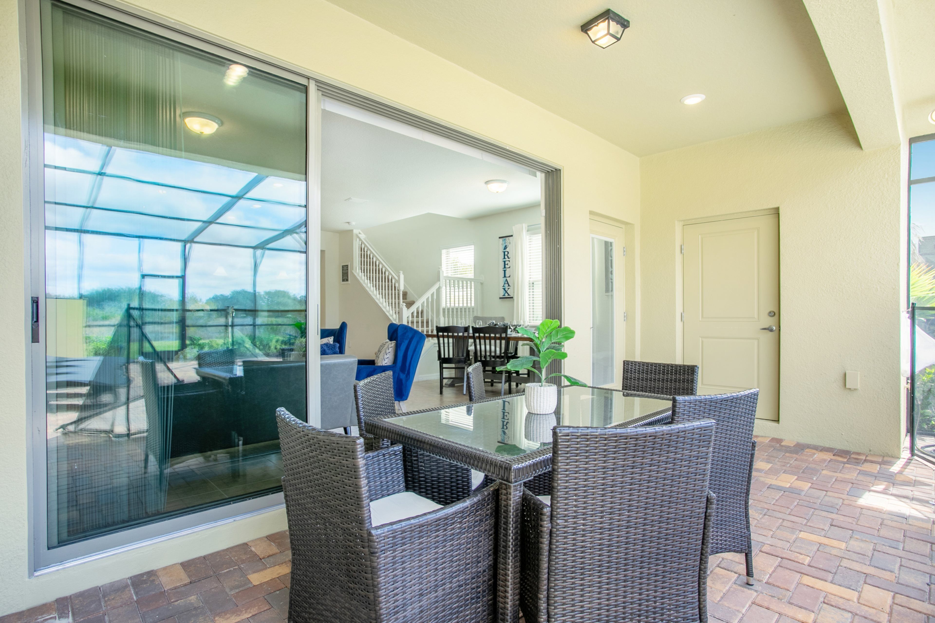 A patio area with a glass table and wicker chairs, a sliding glass door leading to a covered outdoor space, and a staircase to an upper level.