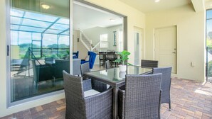 Eine Terrassenfläche mit Glastisch und Korbstühlen, eine Schiebetür zu einem überdachten Außenbereich und eine Treppe zu einer oberen Ebene.