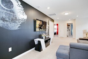 Ein modernes Wohnzimmer mit einem großen Flachbildfernseher an einer schwarzen Wand, einem weißen Konsolentisch und einem grauen Sofa.