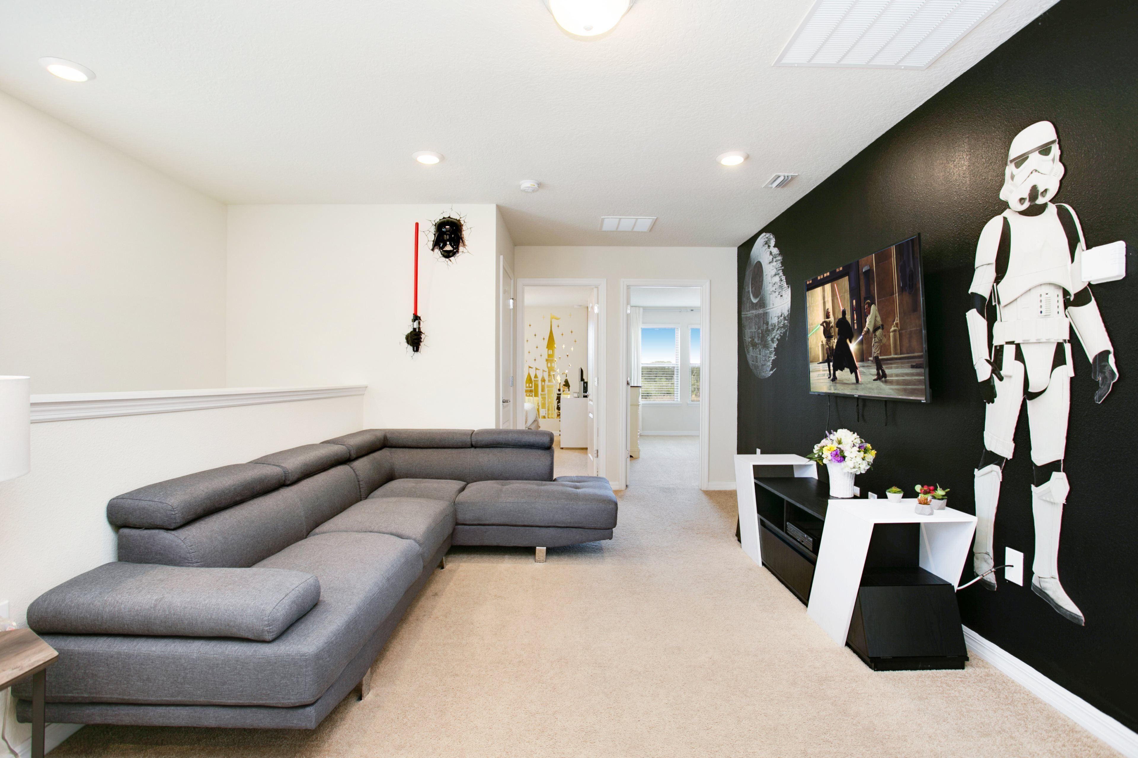A modern living room with a grey sectional sofa, a white coffee table, and a wall-mounted Stormtrooper decoration.
