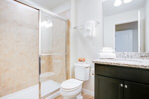 Ein Badezimmer mit Duschkabine aus Glas, Toilette, Waschbecken mit Spiegel und Handtuchhalter.