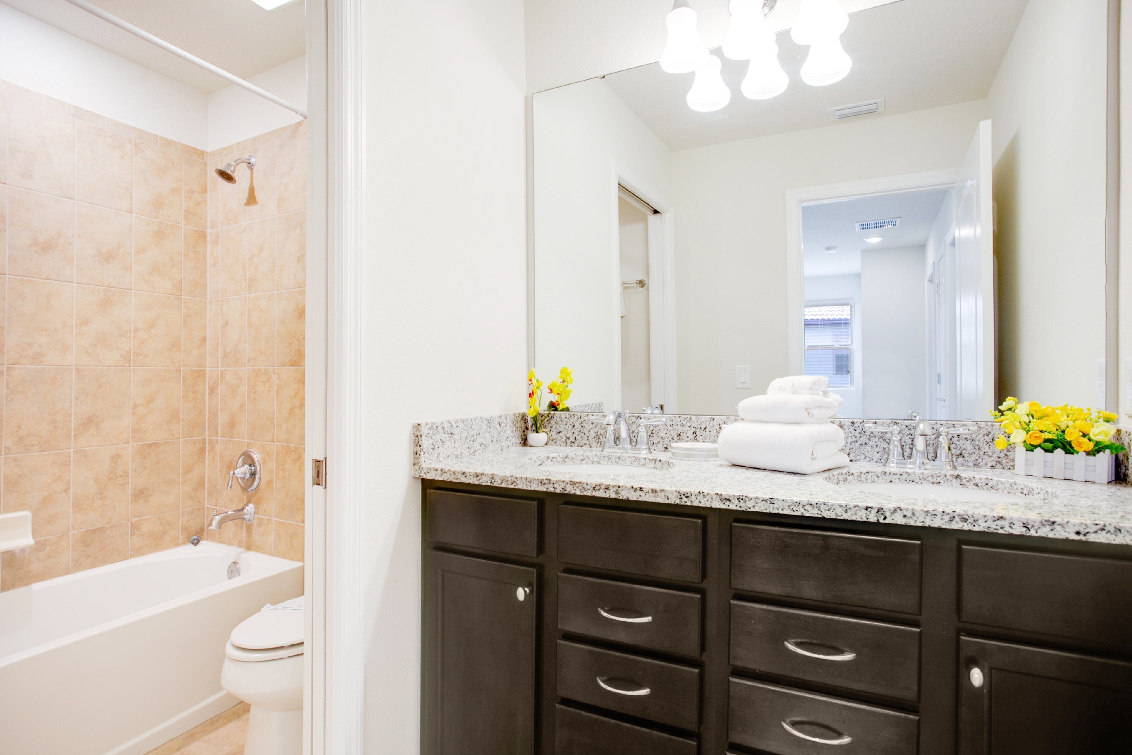 A modern bathroom with a bathtub, a toilet, dark cabinets, a granite countertop, and a mirror.
