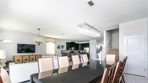 Un comedor moderno con una mesa larga y sillas, una cocina al fondo y una escalera que sube a otro nivel.
