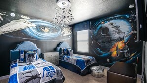 Un dormitorio con dos camas, un ventilador de techo y un mural con motivos espaciales.